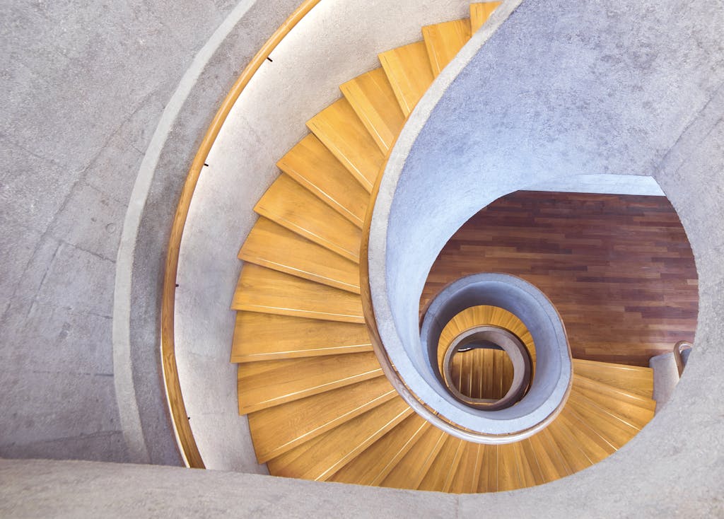 Aerial view of a stylish spiral staircase with wooden steps and a concrete interior.